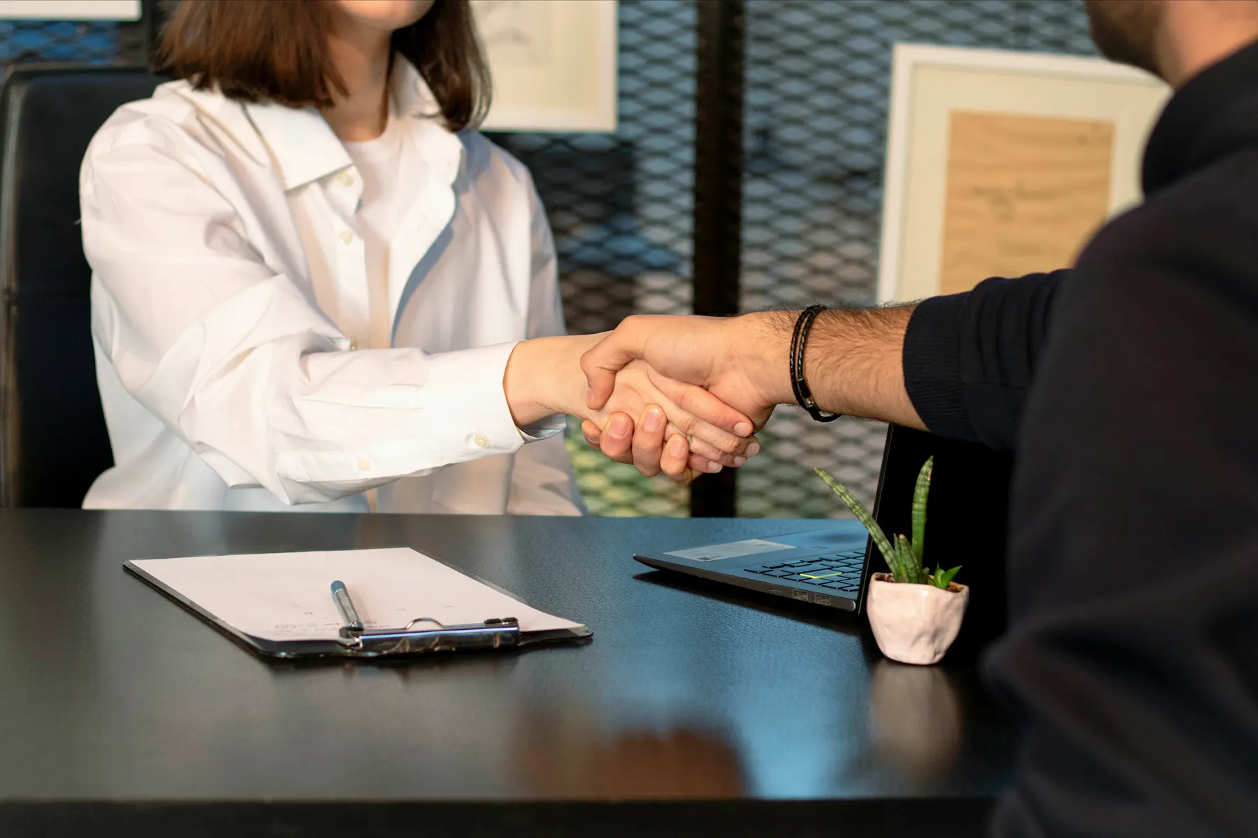 Zwei Personen besiegeln eine Zusammenarbeit per Handschlag am Schreibtisch